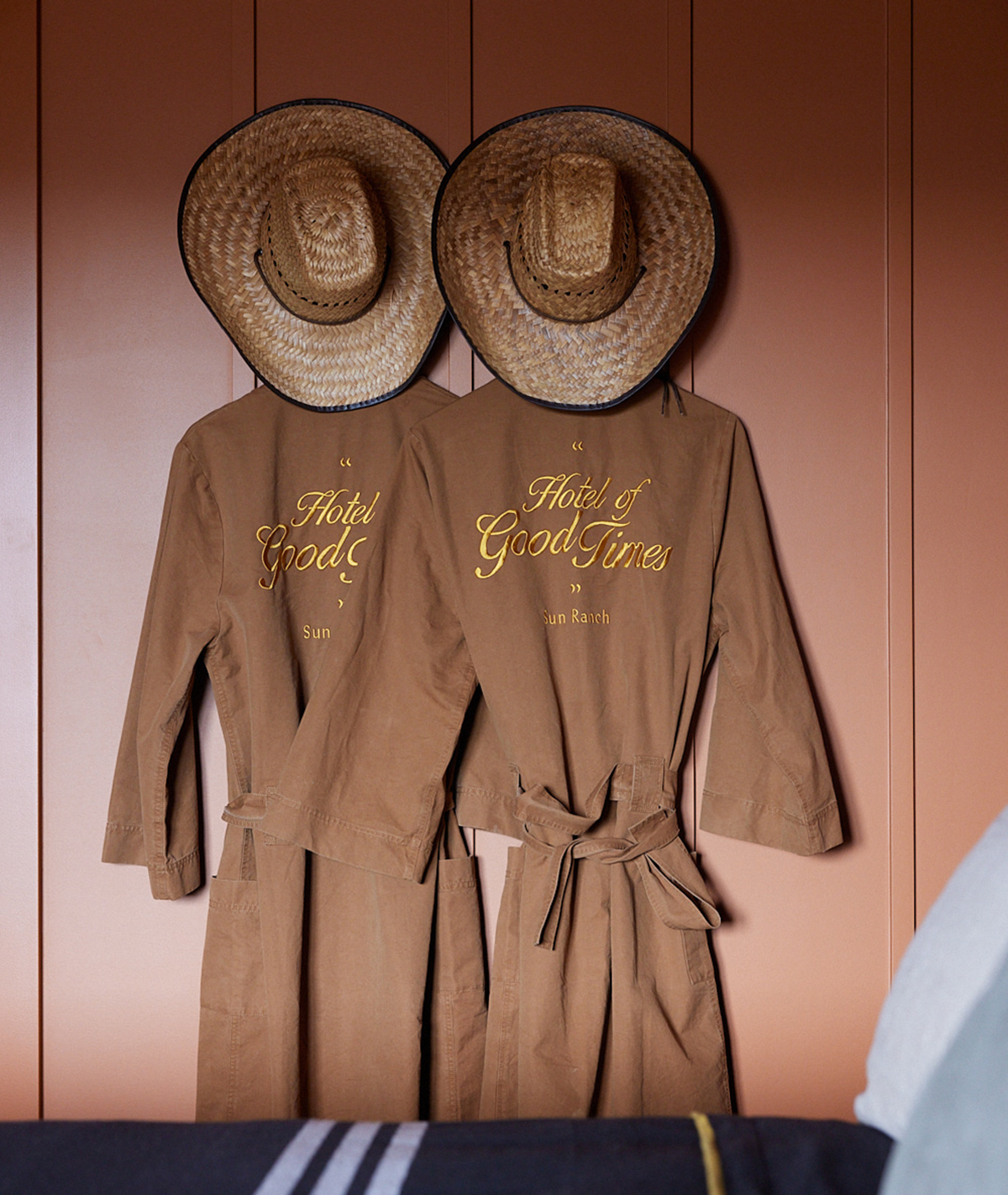 Tan cavas robe hanging on burnt orange bedroom wall with two cowboy hats