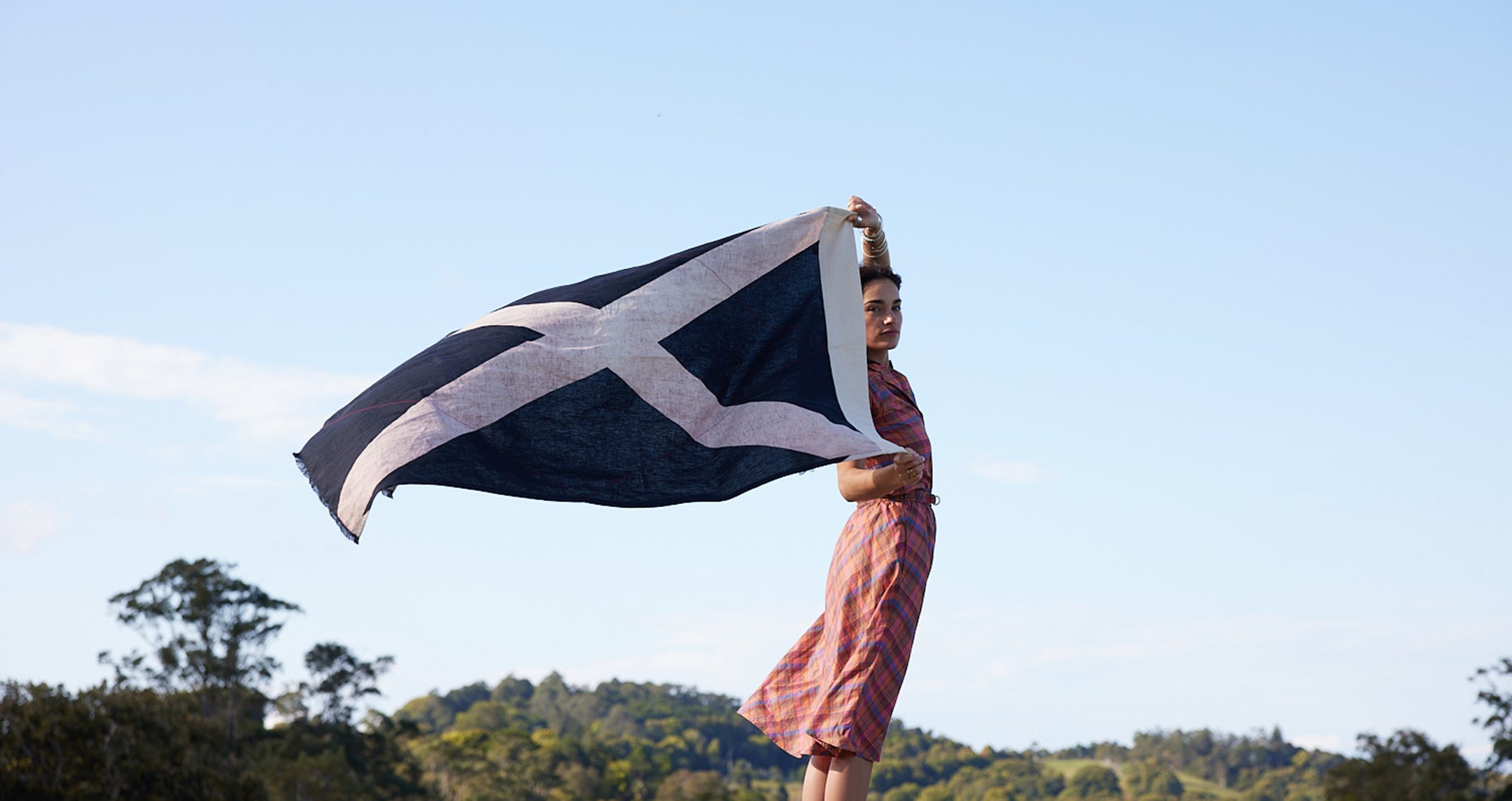 Woman holding black and white x flag behind her head blowing in the wind. Blue sky in background